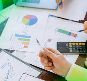 Mesa com gráficos, documentos, laptop e calculadora, com duas pessoas analisando dados financeiros e de mercado, simbolizando o trabalho analítico e estratégico da Agência War em marketing digital baseado em dados.