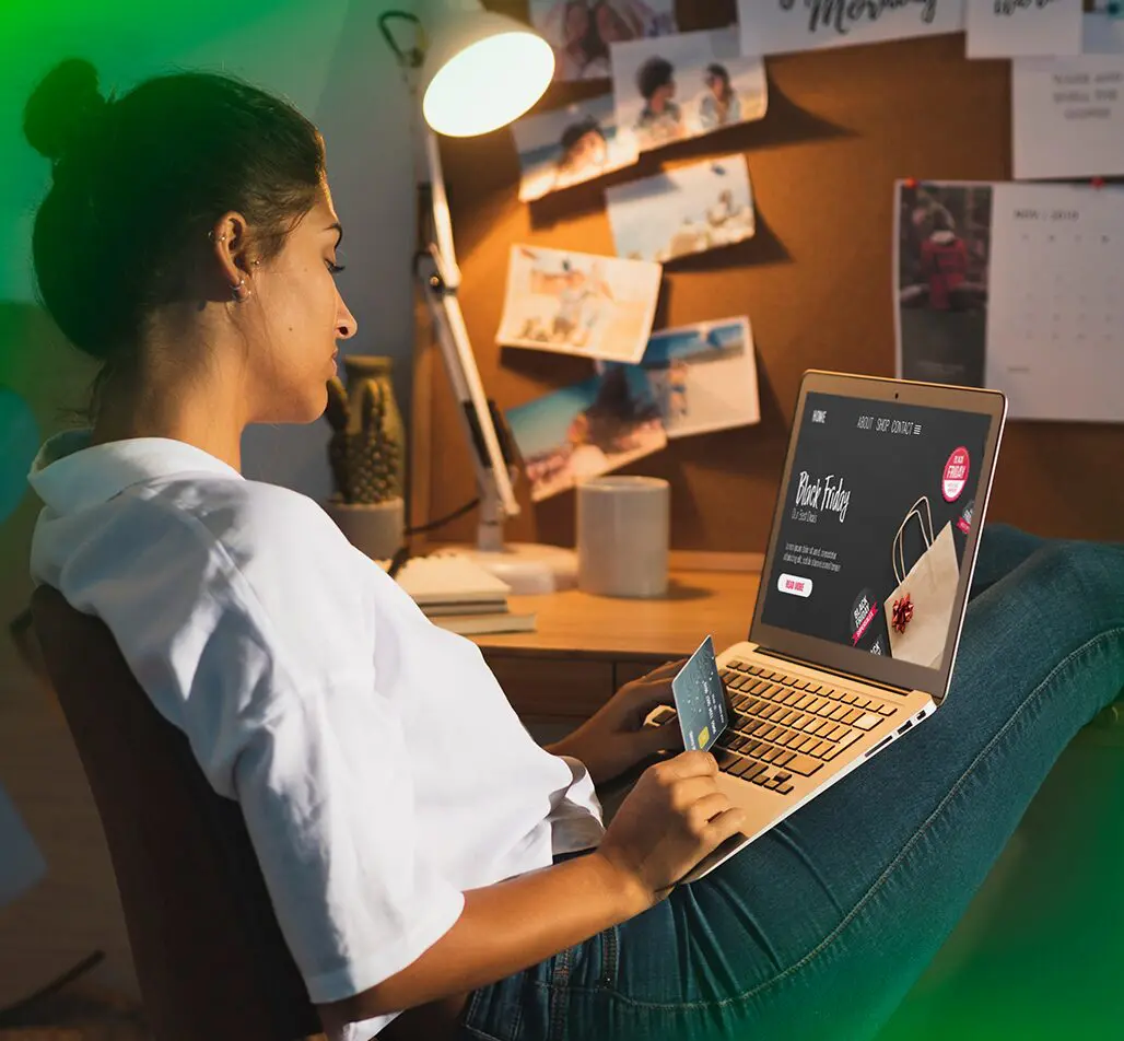 Mulher sentada em frente ao laptop com cartão de crédito na mão, navegando em uma página de promoção de Black Friday, simbolizando o comportamento de compras online e a importância de campanhas promocionais eficazes.