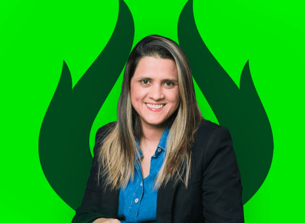 Mulher sorridente usando blazer preto e camisa azul, com fundo verde estilizado, transmitindo energia e profissionalismo.