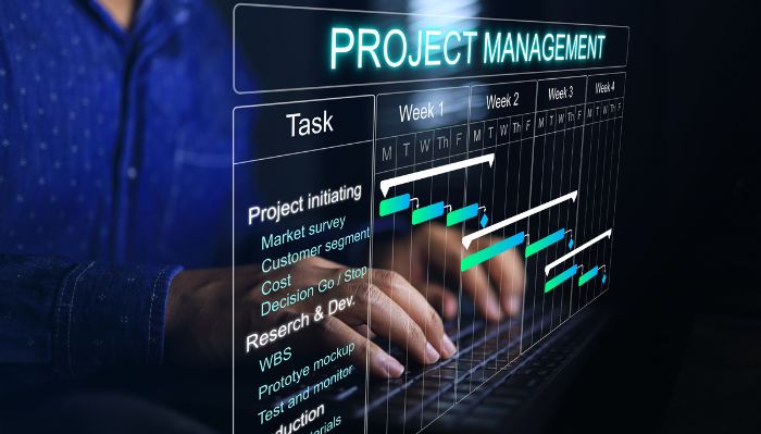 Pessoa digitando em um teclado enquanto interage com um gráfico de Gantt, mostrando tarefas, semanas e barras de progresso, representando o gerenciamento de projetos.